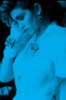 A vintage image of Madonna in a contemplative pose, surrounded by people, used in a TeachRock lesson on the history of music videos, highlighting the evolution of sound and image in media.